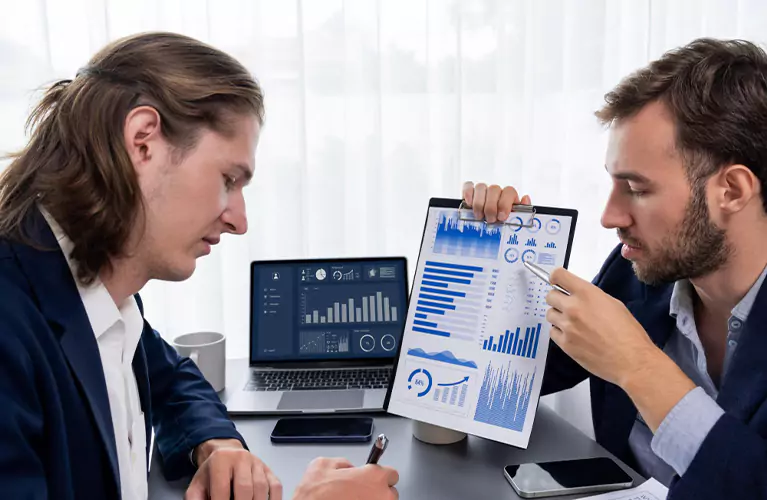 Professionals reviewing charts on a tablet with business reports on a table